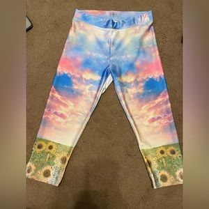 Kids caprees, has a multi colored pattern and sunflowers at the bottom of pants.